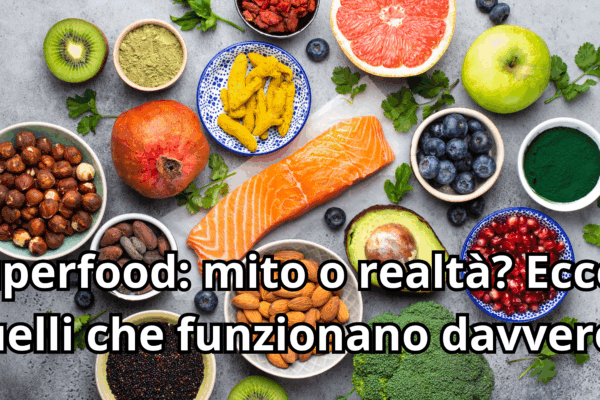 Composizione di vari superfood su sfondo scuro: trancio di salmone fresco, avocado, mirtilli, kiwi, broccoli, frutta a guscio, polveri di tè matcha e semi di chia. Al centro compare il titolo dell'articolo: Superfood: mito o realtà?