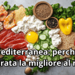 Vista dall'alto di un ricco tagliere in legno che presenta i pilastri della dieta mediterranea: tranci di carne magra, gamberi, uova, formaggio fresco, pomodori ciliegino, cetrioli, peperoni gialli, noci, uva, aglio e cereali, il tutto arricchito da erbe aromatiche fresche. In primo piano il titolo: 'Dieta Mediterranea: perché è considerata la migliore al mondo'.